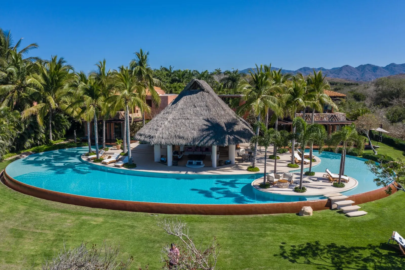 Aerial view of the lagoon pool wrapped around the thatched palapa, the Sierra Madre behind