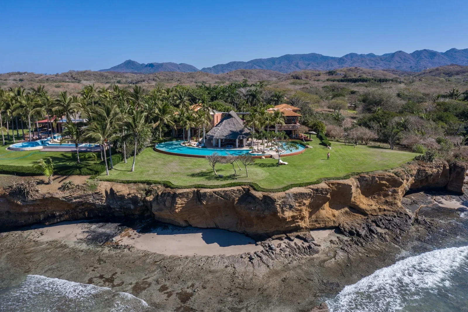 The lawn, palms and pool on the cliff edge, with the surf breaking on the reef below