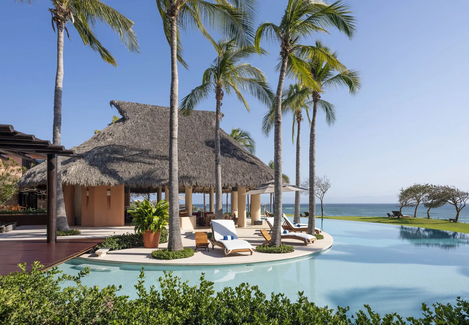 Loungers on a palm-shaded island in the pool, the ocean beyond the terrace