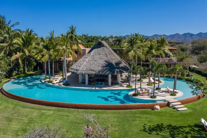 Aerial view of the lagoon pool wrapped around the thatched palapa, the Sierra Madre behind