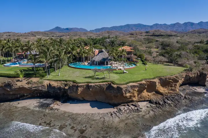 The lawn, palms and pool on the cliff edge, with the surf breaking on the reef below