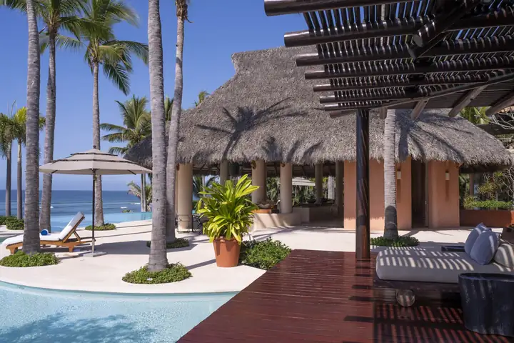 A shaded deck with daybeds beside the pool and the palapa