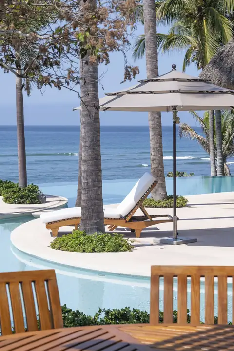 A sun lounger under an umbrella at the pool's infinity edge, the sea beyond