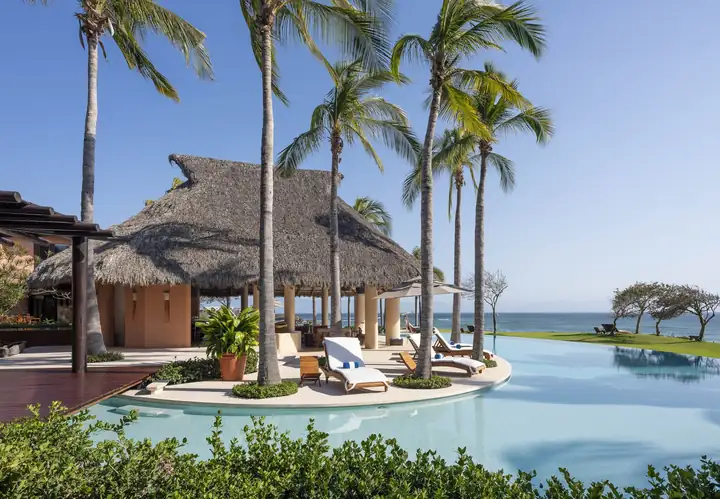 Loungers on a palm-shaded island in the pool, the ocean beyond the terrace