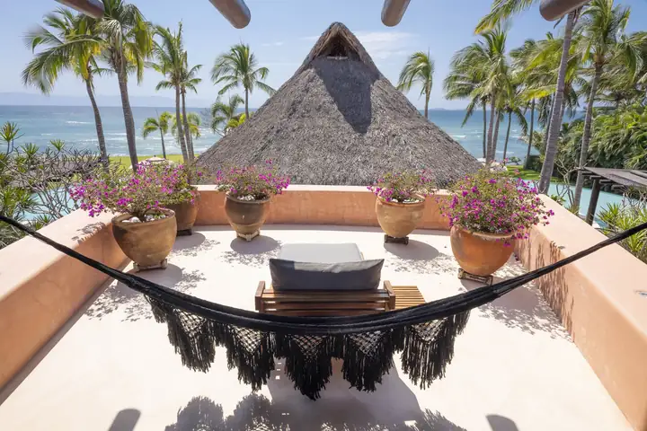 A hammock on an upper terrace with bougainvillea and the ocean beyond the palapa roof